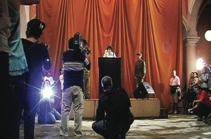 Tatlin’s Whisper #6 (Havana Version), 2009. Stage, podium, microphone, loudspeakers, curtain, 2 people in military fatigues, dove, audience, and 200 disposable cameras, Wilfredo Lam Center, Havana. Courtesy of Berezdivin Collection, San Juan, Puerto Rico. El susurro de Tatlin #6 (version para La Habana), 2009. Plataforma, podio, micrófonos, baffles, telón, dos personas con vestimenta militar de faena, paloma, público y 200 cámaras desechables. Centro Wifredo Lam, La Habana. Cortesía Colección Berezdivin, San Juan, Puerto Rico.